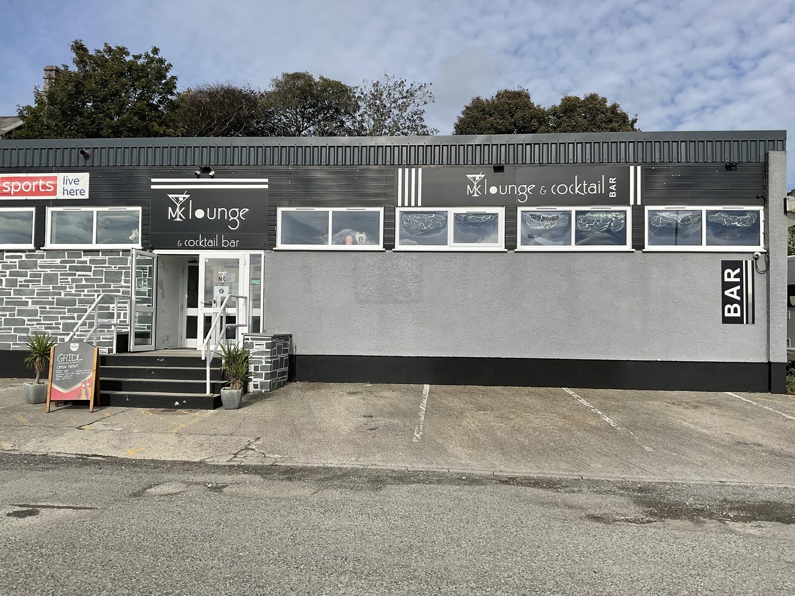 The front of MK Lounge & Cocktail Bar on Omaha Road, Bodmin, with the GRIDL A-board by the entrance steps and marked parking bays outside
